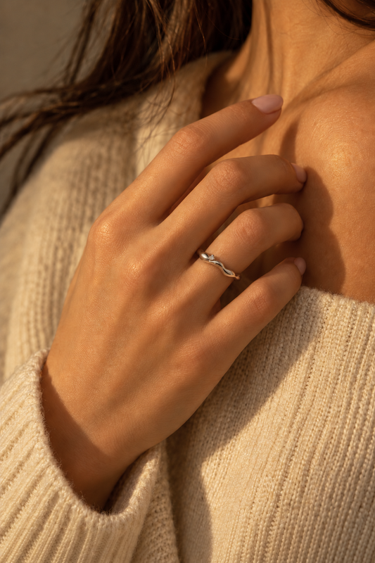 Milk & Rose Pamela Ring with a wavy silver-tone outline, worn on a hand at the neckline of a cream knit sweater.