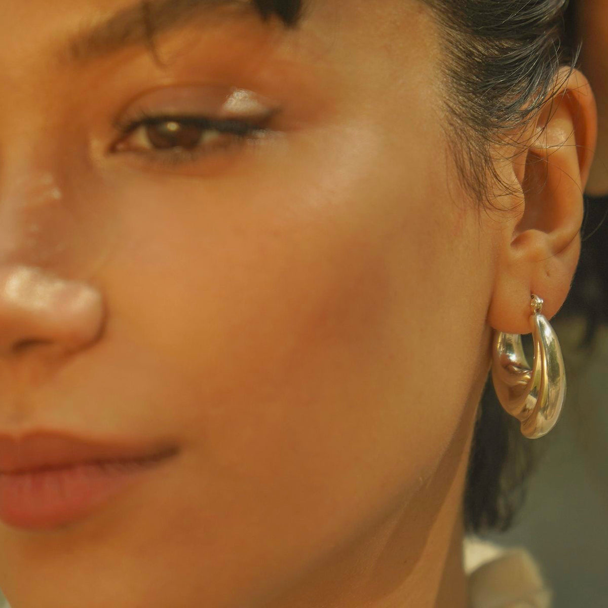 Close-up of Milk & Rose Aura Hoops worn on the ear, showing their sculptural layered curves beside the face.