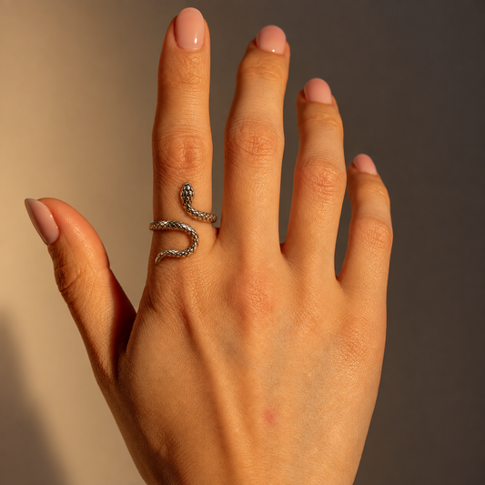 Milk & Rose Egypt Ring worn on an index finger, showing its textured snake shape curling around the finger against a warm beige background.