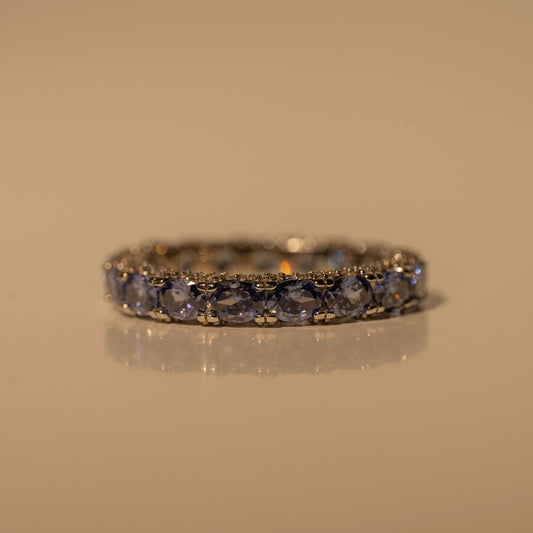 Glamband Ring with blue-purple stones and small clear accents, resting flat on a beige surface