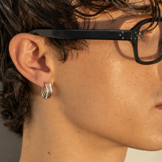 Close-up of a Milk & Rose Eve Hoop worn beside black-framed glasses, showing its silver-tone angular curve.