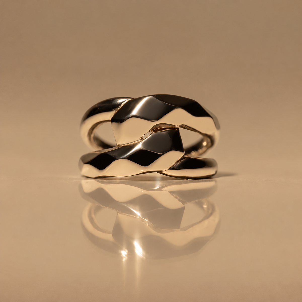 Front view of the Milk & Rose Bold Unity Ring, a polished gold-tone double band with two overlapping faceted wave-shaped sections, on a reflective beige surface.