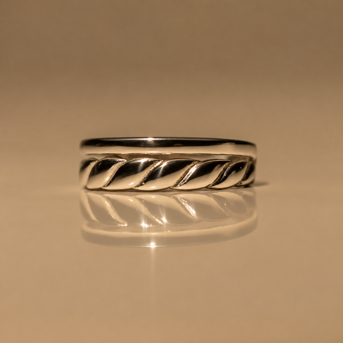 Front view of the Milk & Rose Braid Adjustable Ring, a polished silver-tone band with a twisted rope braid detail along the front, on a reflective beige surface.