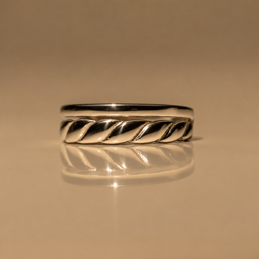Front view of the Milk & Rose Braid Adjustable Ring, a polished silver-tone band with a twisted rope braid detail along the front, on a reflective beige surface.