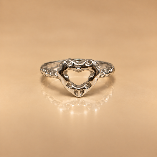 Milk & Rose Hammered Heart Ring in sterling silver, open heart design with hammered texture, on a warm beige background