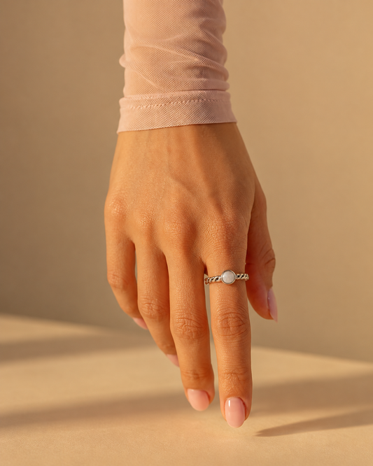 Ribbon Pearl Ring worn on a hand, sterling silver braided band with a round mother of pearl stone
