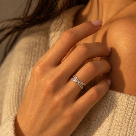 Milk & Rose Lisette Ring worn on a hand near a cream knit sweater, showing its silver-tone crossing bands and clear stones.