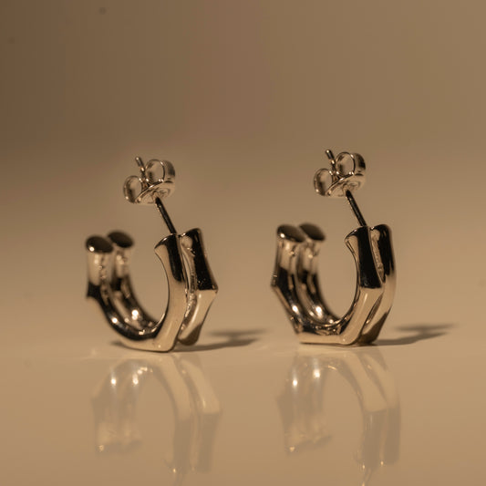 Milk & Rose Eve Hoops in a silver tone, with flat angular curves and butterfly backs, standing together on a reflective surface.