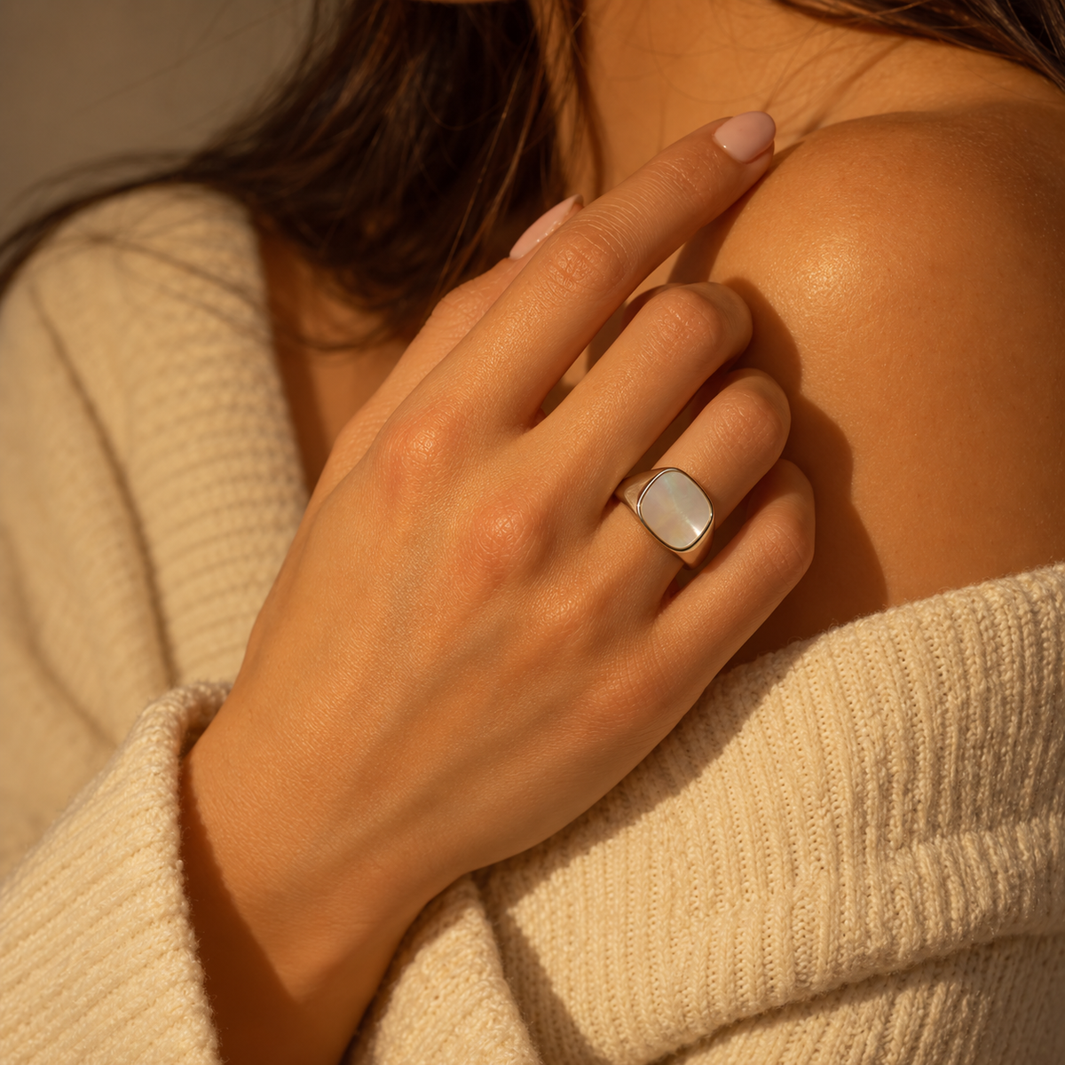 Milk & Rose Kare Pearl Ring worn on a hand resting at the shoulder above a cream knit sweater, showing its pale pearly face and silver-tone frame.