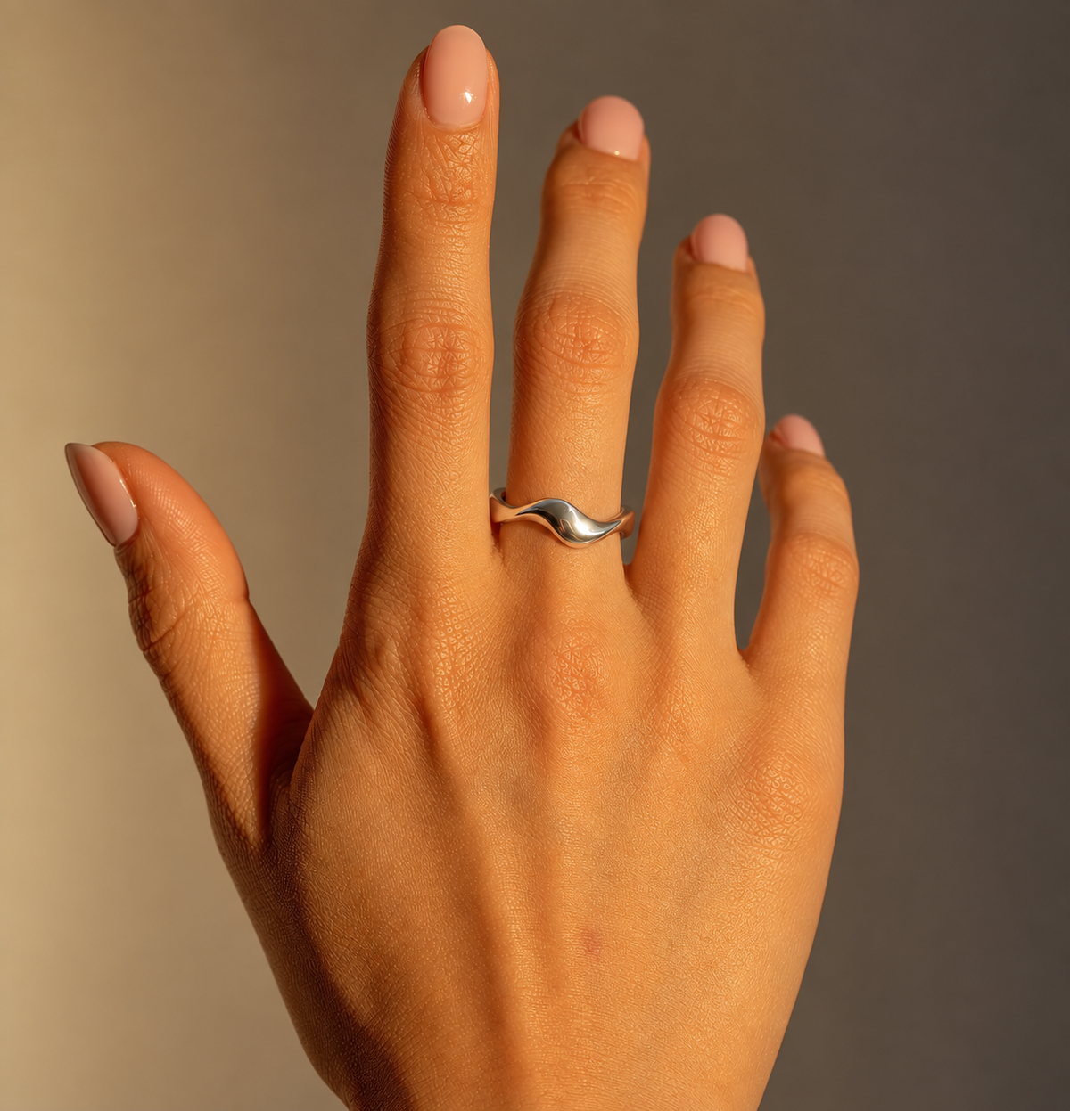 Milk & Rose Twist Ring worn on a hand with pale pink nails, showing the polished silver-tone band and flowing wave detail in warm light.