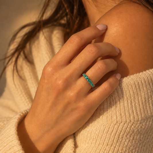 Emerald Eternity Ring worn on a hand resting against a cream knit top, with a row of round green stones across the finger.