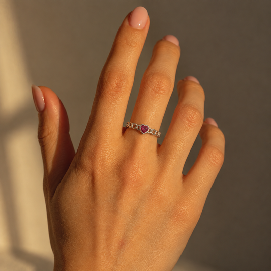 Milk & Rose Middle Heart Ring worn on a hand in warm sunlight, with a pink heart-shaped center and a silver-tone linked band.