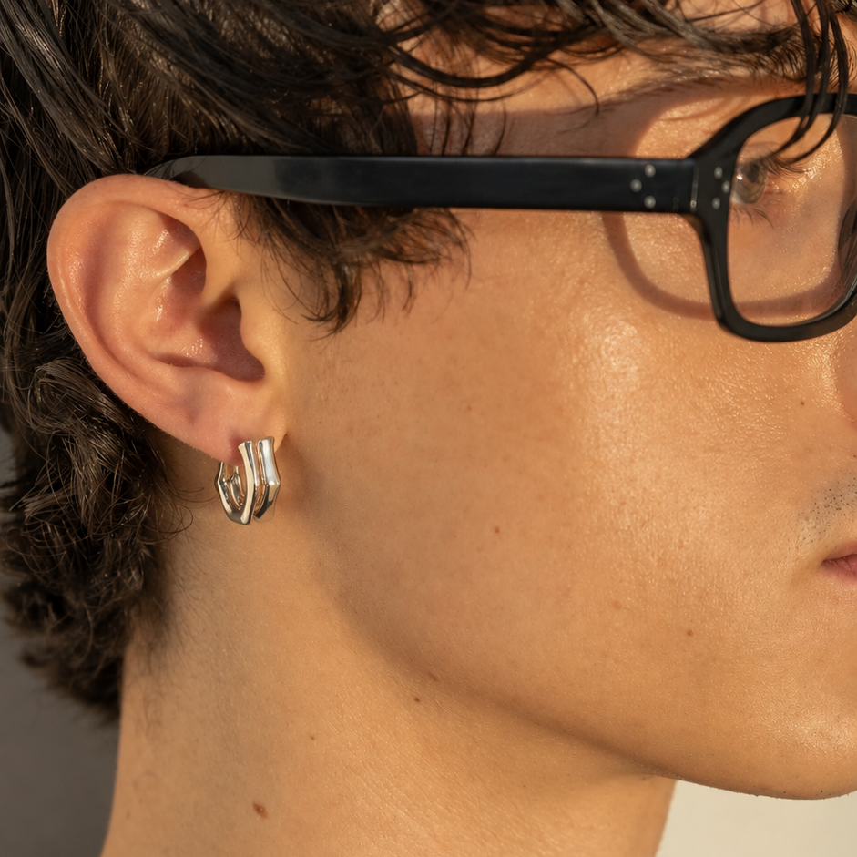 Close-up of a Milk & Rose Eve Hoop worn beside black-framed glasses, showing its silver-tone angular curve.